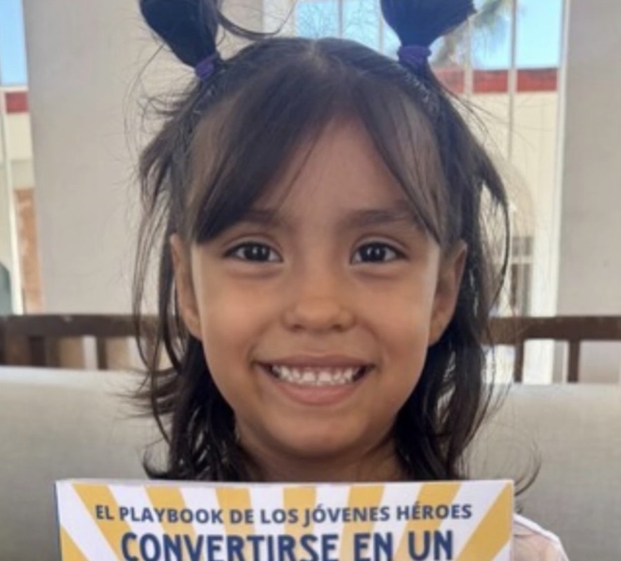 A young girl smiling and holding the Spanish Young Heroes Playbook