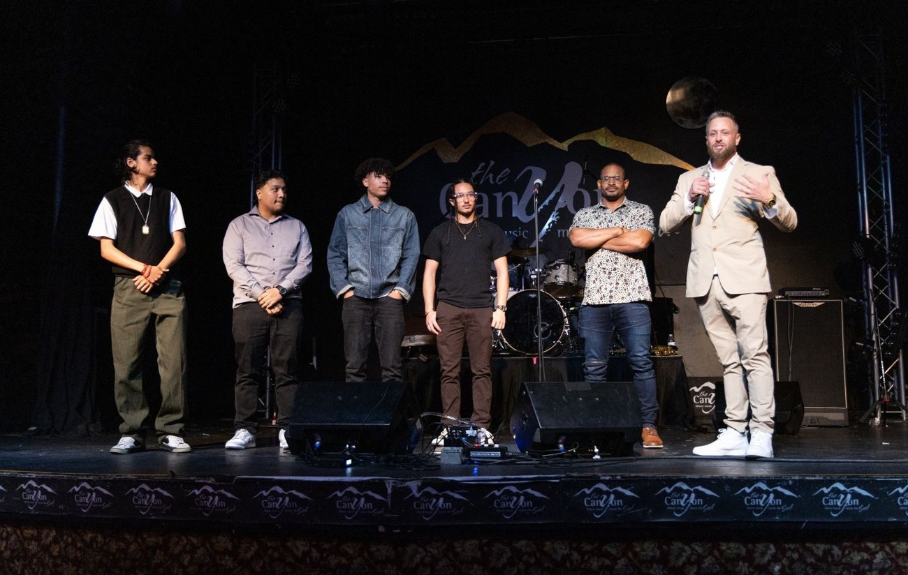 Jason Hill, Güerote, speaking on stage alongside a group of young men